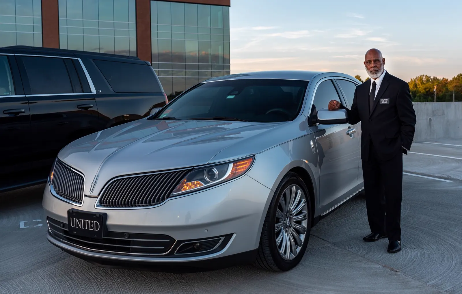 Professional chauffeur standing beside a luxury sedan